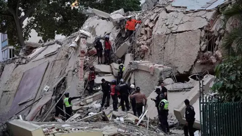 AFP via Getty Images About a dozen rescuers search for victims amidst a building that's been reduced to rubble following an earthquake in Caracas 