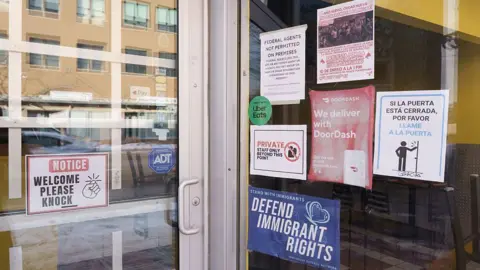 Bloomberg via Getty Images a bunch of signs on a storefront advocating for immigrants and saying no ICE allowed