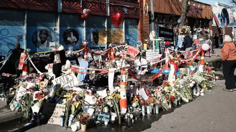 Getty Images A memorial to Alex Pretti, full of flowers and candles on a sidewalk, set up at the location where federal agents shot and killed him