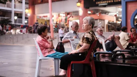 Getty Images Old people sitting on plastic chairs in an open space