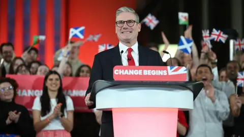 AFP via Getty Images Sir Keir beams at a lectern with the banner that reads "change begins". 