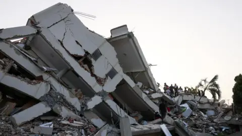 Reuters A large, crumbled building with a group of people climbing onto it.