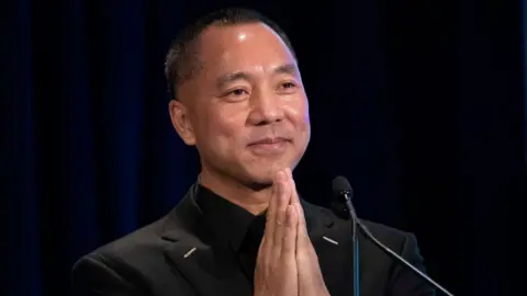 AFP via Getty Images Chinese billionaire Guo Wengui places his hands together while speaking on stage during a news conference in 2018 in New York