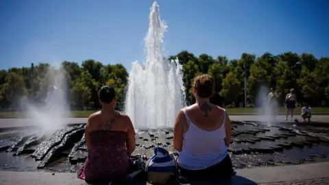 EPA/Shutterstock Two women look at a fountain on a sunny day with their backs to the camera