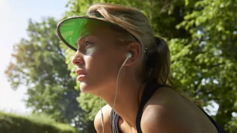 Getty Images A young woman with a green visor and white earbuds squints into the distance in the countryside