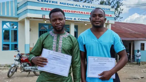 Reuters 


Makati Tagirabo,34, and Baraka Bulambula 29, Congolese health workers who recovered from the Ebola virus hold their certificates of discharge at the Evangelical Medical Center (CEM), as agencies intensify efforts to contain a new Ebola outbreak caused by the Bundibugyo virus strain, in Bunia, Ituri province, Democratic Republic of Congo, May 31, 2026. REUTERS/Gradel Muyisa Mumbere