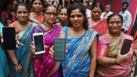 Hindustan Times via Getty Images Women who were beneficiaries of a government cash transfer scheme showing their bank passbooks and the message of the scheme money received on their mobile phones in Maharashtra, India - 2024. 