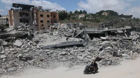 EPA A man riding a motorcycle past destroyed buildings in the village of Mayfadoun, southern Lebanon (23 June 2026)