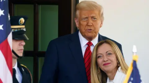 EPA-EFE/REX/Shutterstock The Italian leader with blonde hair on the right smiles at the camera while the US president in a blue jacket asnd red tie stands behind her and looks at the camera
