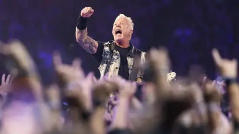 Getty Images Metallica front man, James Hetfield, punches the air wearing a waistcoat, black T-shirt and wrist sweat band with short blonde hair
