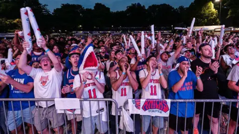 Getty Images a crowd of fans wearing Knicks gear gather in a park to watch one of the finals games