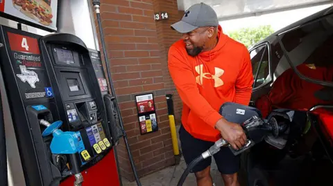 The Dallas Morning News via Getty Images A man in a red hoodie refuels his car while keeping an eye on the price display.