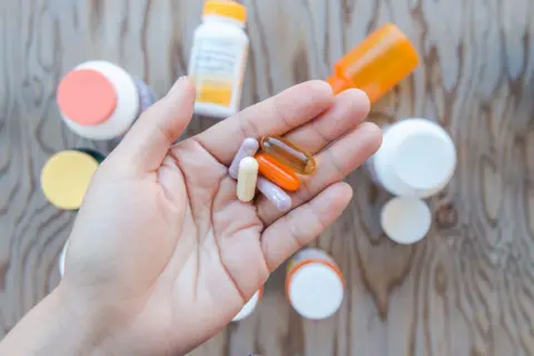 Getty Images A hand holding a bunch of supplements in an open palm. There are bottles of supplements as a background.