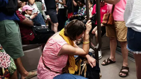 Getty Images A woman sits on the floor of a crowded carriage on metro line 11 during a heatwave in Paris