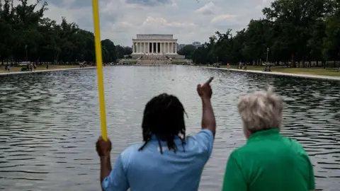 Getty Images A worker provides a visitor with directions as he cleans the waters of the Lincoln Memorial Reflecting Pool following the completion of recent renovations in Washington, DC, on June 22, 2026. 