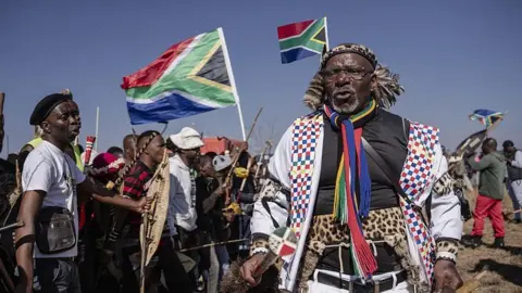Anadolu via Getty Images Hundreds of protesters marching outdoors, chanting and holding south african flags and signs