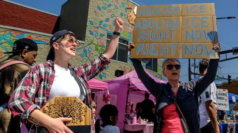 AFP via Getty Images protesters hold up signs, one says "abolish ICE right now" during a parade