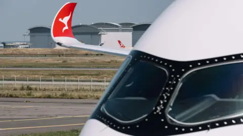 Qantas A close up of an airplane's cockpit, with the wingtip visible in the distance with the red and white kangaroo logo of Qantas.