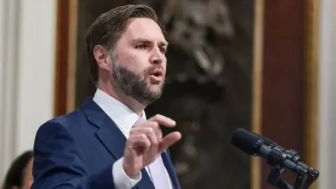 Reuters JD Vance speaking into a microphone. 
