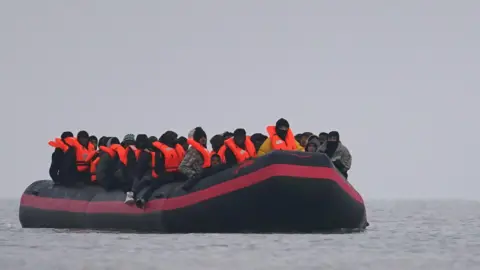 PA Media A small inflatable boat is on the water with a number of people wearing inflatable life jackets