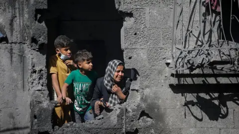 EPA File photo showing Palestinian children looking out from their family's destroyed house following an Israeli air strike, in Shati refugee camp, northern Gaza (29 October 2025)