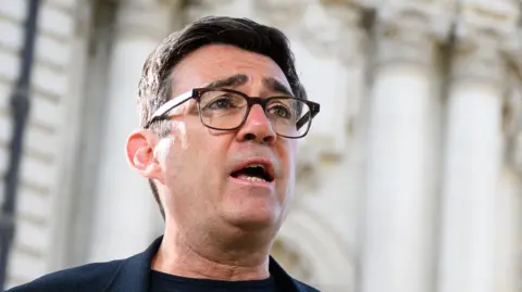 Getty Images Andy Burnham is wearing a dark coloured jacket and glasses. 
