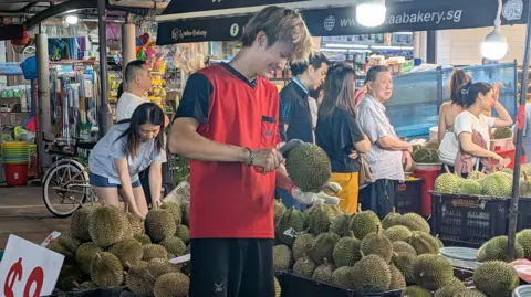 Kelly Ng/ BBC A fruit seller cutting durian at a stall