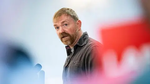 Getty Images Graham Platner looks toward the camera, framed by campaign posters. 