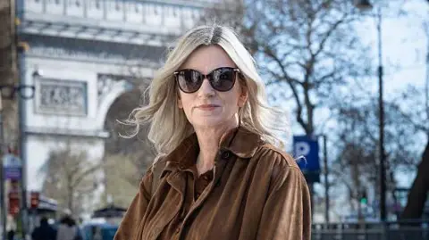 AFP via Getty Images Lisa Bankworth, wearing shades and a brown jacket, poses for a photograph in Paris on 18 March 2026