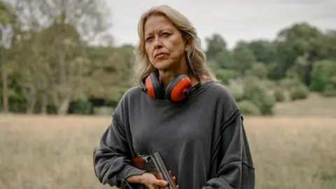 Disney Nicola Walker as Alice holding a shotgun in her hand 