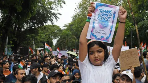 AFP A young girl holds a placard as citizens gather to celebrate the resignation of Union Education Minister Dharmendra Pradhan. 