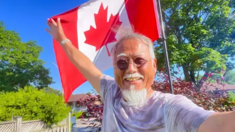 Dong Guangping Dong Guangping posing in front of a Canadian flat, with his right hand holding the flag
