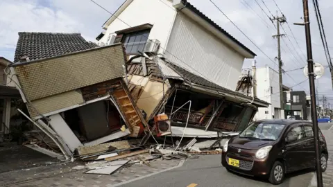 Reuters A small brown car sits on the street beside a collapsed house