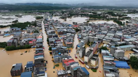 Reuters Aerial view of homes and buildings submerged in brown flood waters in Hengzhou, Nanning, China with a green mountain range and clody skies in the background