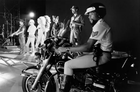 Getty Images Victor Willis sits on a motorcycle as the rest of the Village People perform on stage