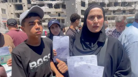 Umm Samir al-Dini (R) stands next to her son Muath, who is using crutches (L), outside al-Shifa hospital in Gaza City, northern Gaza
