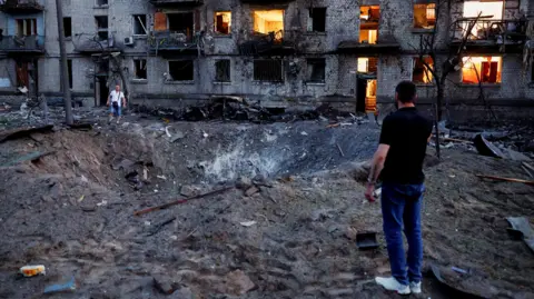 Reuters Residents stand next to a crater formed at a site during overnight Russian missile and drone strikes, amid Russia’s attack on Ukraine, in Kyiv, Ukraine on 2 July.