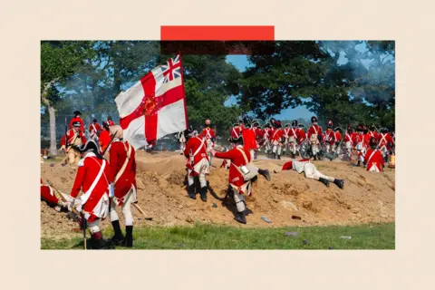 Getty Images A group of men wearing red and white uniforms climb a sandbank as part of a battle re-enactment