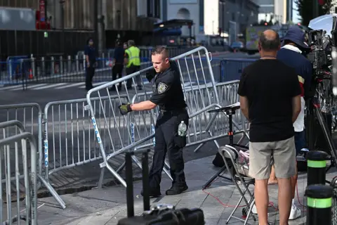 Getty Images A police officer places a metal barricade on the streets around Madison Square Garden while a TV crew looks on.