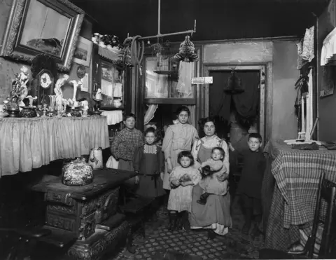Getty Images Black and white photo of Immigrant family in New York City. Mother is seated holding baby on her lap
