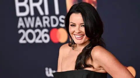Getty Images A woman with long black hair is smiling while wearing a black dress. She appears to be on a red carpet at the BRIT awards.