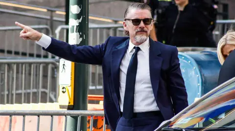 Getty Images Ethan Hawke pictured wearing a navy suit. His arm is outstretched and his finger is pointed 