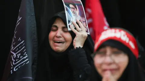 Reuters A woman appears to cry as she attends Ayatollah Khamenei's funeral holding a poster of him.