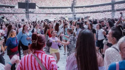 Live Nation/PA Fans, many female and wearing sparkly skirts and dresses, can be seen dancing in the standing area of Wembley Stadium during Styles' concert on Saturday. Thousands of other people can be seen in the background