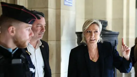 AFP via Getty Images Marine Le Pen gestures as she arrives after a break in the defense's closing argument in the trial of far-right party Rassemblement National (RN) former or actual members on charges of embezzlement of European public funds in a case of alleged European Parliament fake jobs at the Palais de Justice in Paris on February 4, 2026