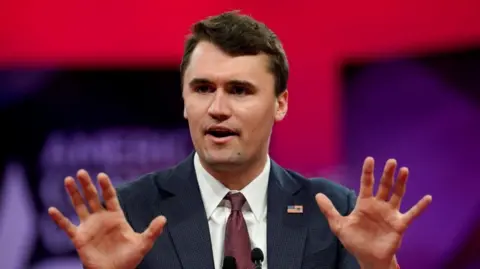 Reuters Charlie Kirk gestures with his hands as he talks in front of a red and purple background