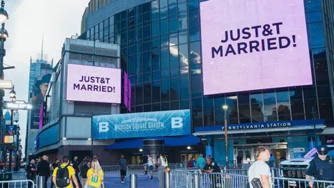 Getty Images A sign outside New York's Madison Square Gardens confirming Taylor and Travis got married. It says "Just T&T Married" on a large screen, with barriers in front and people hanging around outside