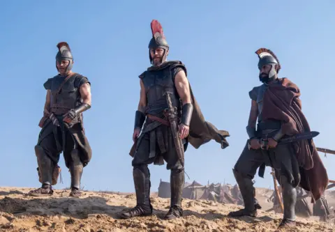 Universal Pictures (L-R) Jimmy Gonzales as Cepheus, Matt Damon as Odysseus and Himesh Patel as Eurylochus in their warrior outfits, armoury and swords 