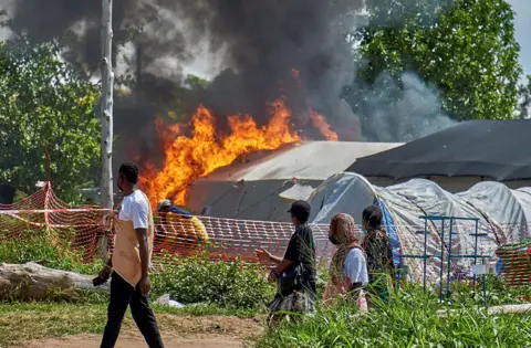 Congolese civilians walk past at the burning Ebola treatment center in Rwampara general hospital in Rwampara outside Bunia, Ituri province