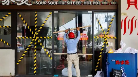 Reuters Qi Pengwen, regional manager of the Youth Coast shopping mall, secures the door of a restaurant with wooden bars